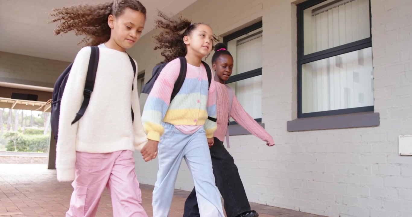 African American children entering walkway holding hands with backpacks passing camera to school