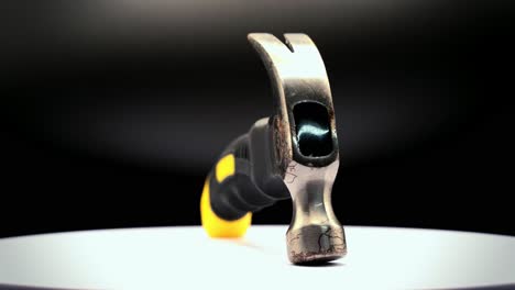close-up static shot of a small rusty claw hammer with black and yellow rubber handle rotating 360 degrees on a platform under studio lighting