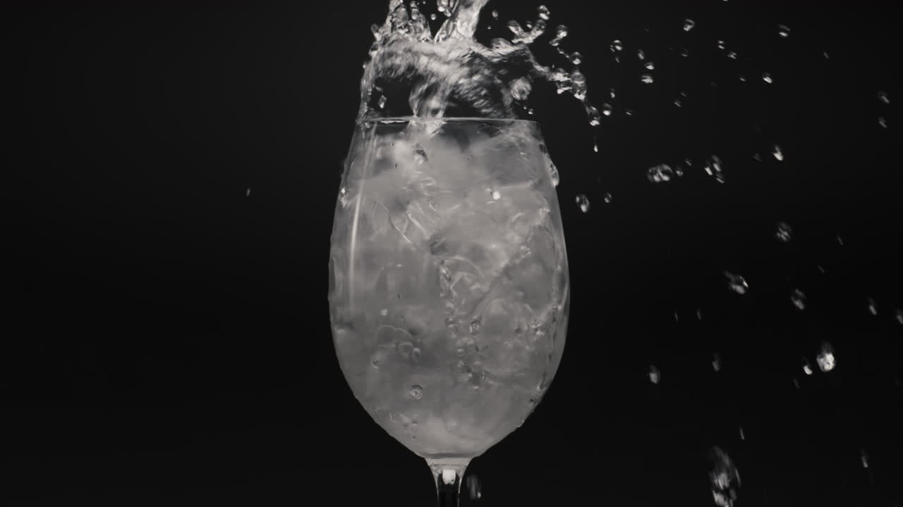 Primo piano di acqua minerale versata in un bicchiere con ghiaccio. Preparazione di cocktail e bevande.