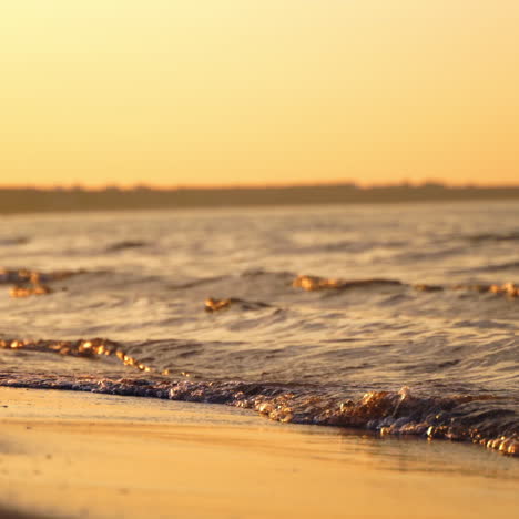 sea water splashes on sand beach in the evening. the edge of the ocean with calm waves on the shoreline at sunset. close-up.