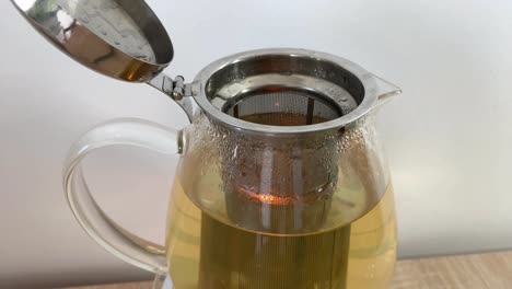 close-up on transparent teapot with oolong tea with removable infuser and candle reflection