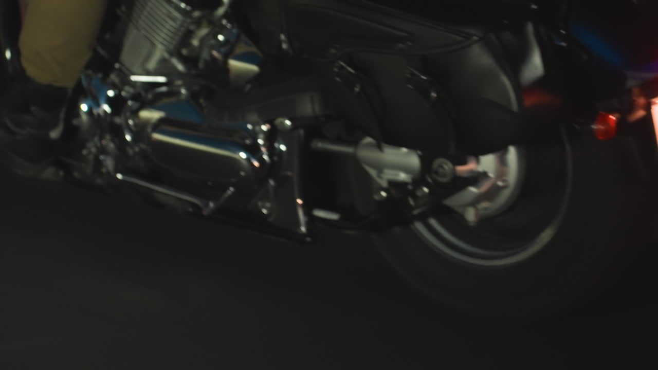 Lower angle view of motorcycle wheel spinning quickly on asphalt during night time, chrome parts reflecting street lights while capturing speed, motion, and intensity of powerful bike on dark road