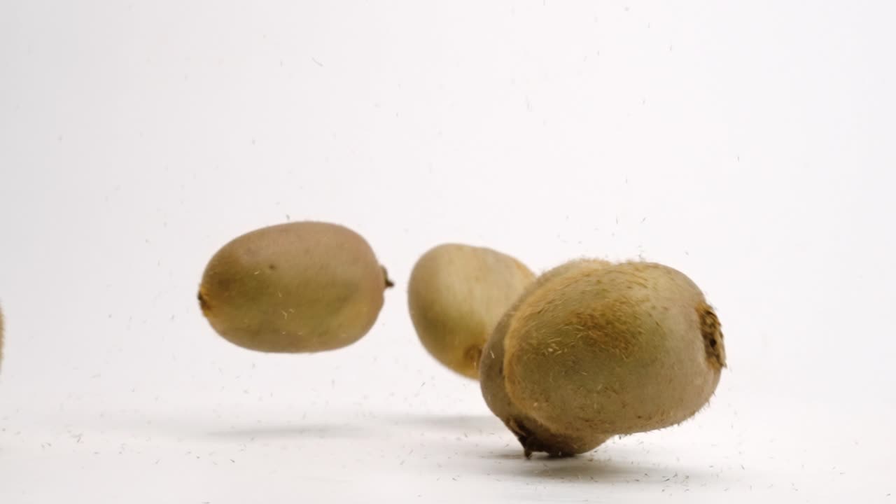 Kiwi interi che cadono e rimbalzano su sfondo bianco da studio in slow motion 4K.