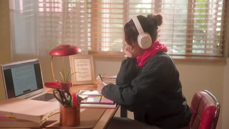 teenage girl listening to music while writing and studying on her desk