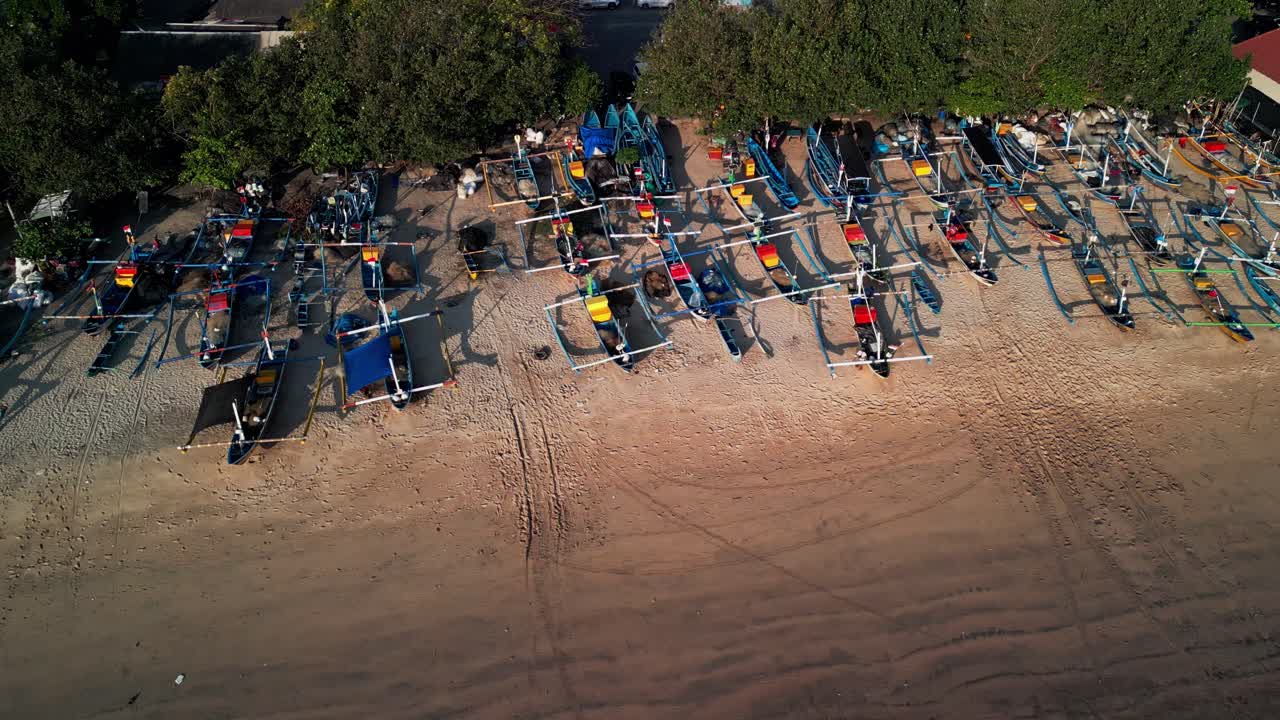 Golden sunset along Bali’s coast illuminates fishing boats arranged on sandy beach, each vessel telling a story of tradition, community, and connection to the sea within a tropical paradise setting