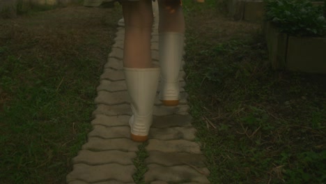 woman walking in garden path in white rain boots