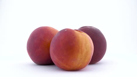 three whole mature peach fruits. rotating on the turntable isolated on the white background. close up. macro.