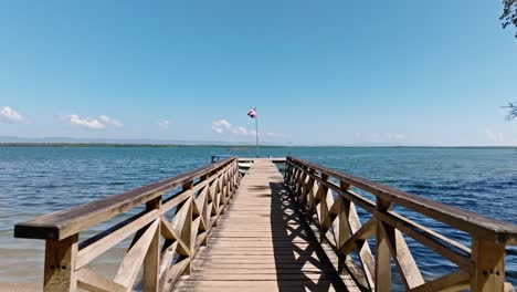 First-person-view-walking-along-wooden-pier-with-Dominican-flag,-San-Lorenzo-bay-in-Los-Haitises-National-Park,-Dominican-Republic
