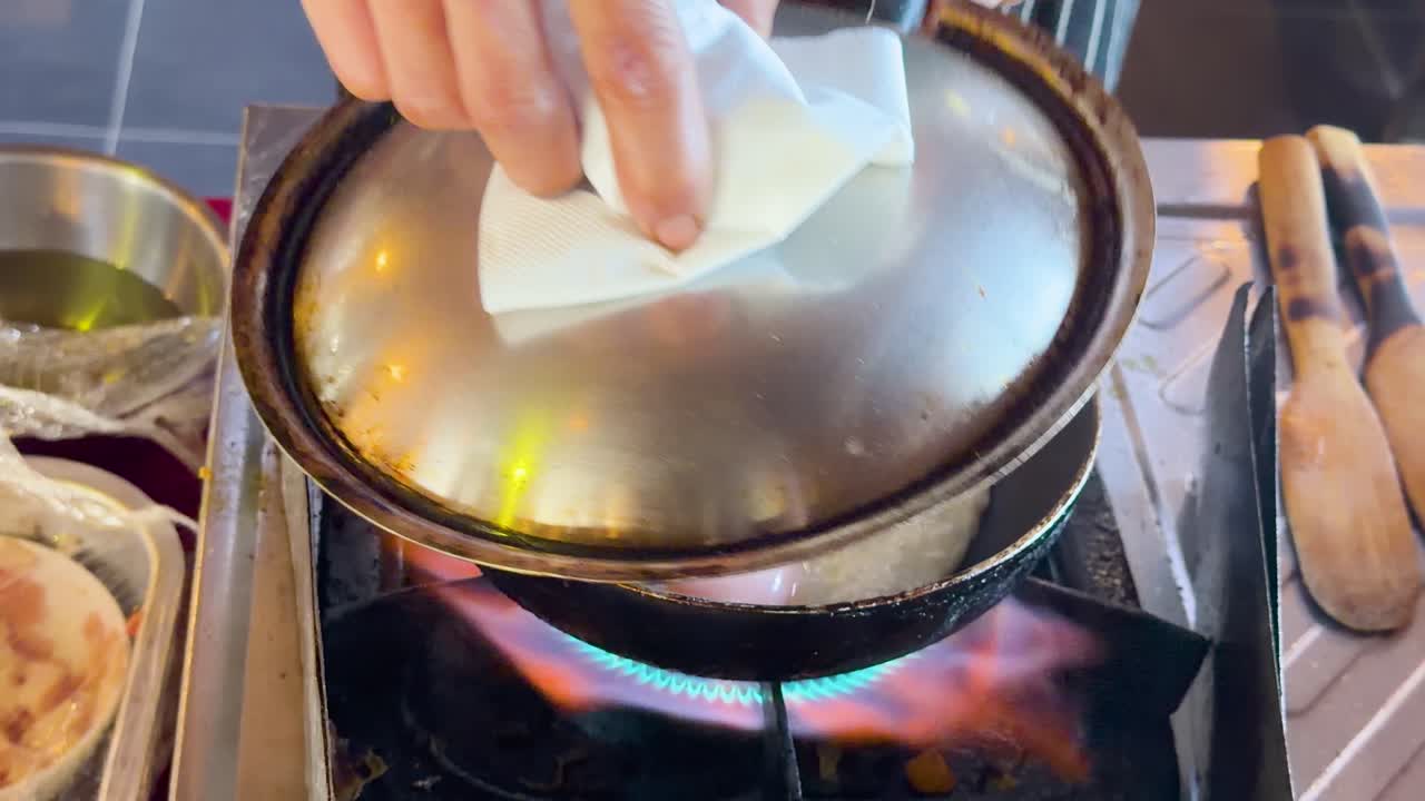 Close-up shot of a chef lifting a lid to reveal frying eggs on street burner