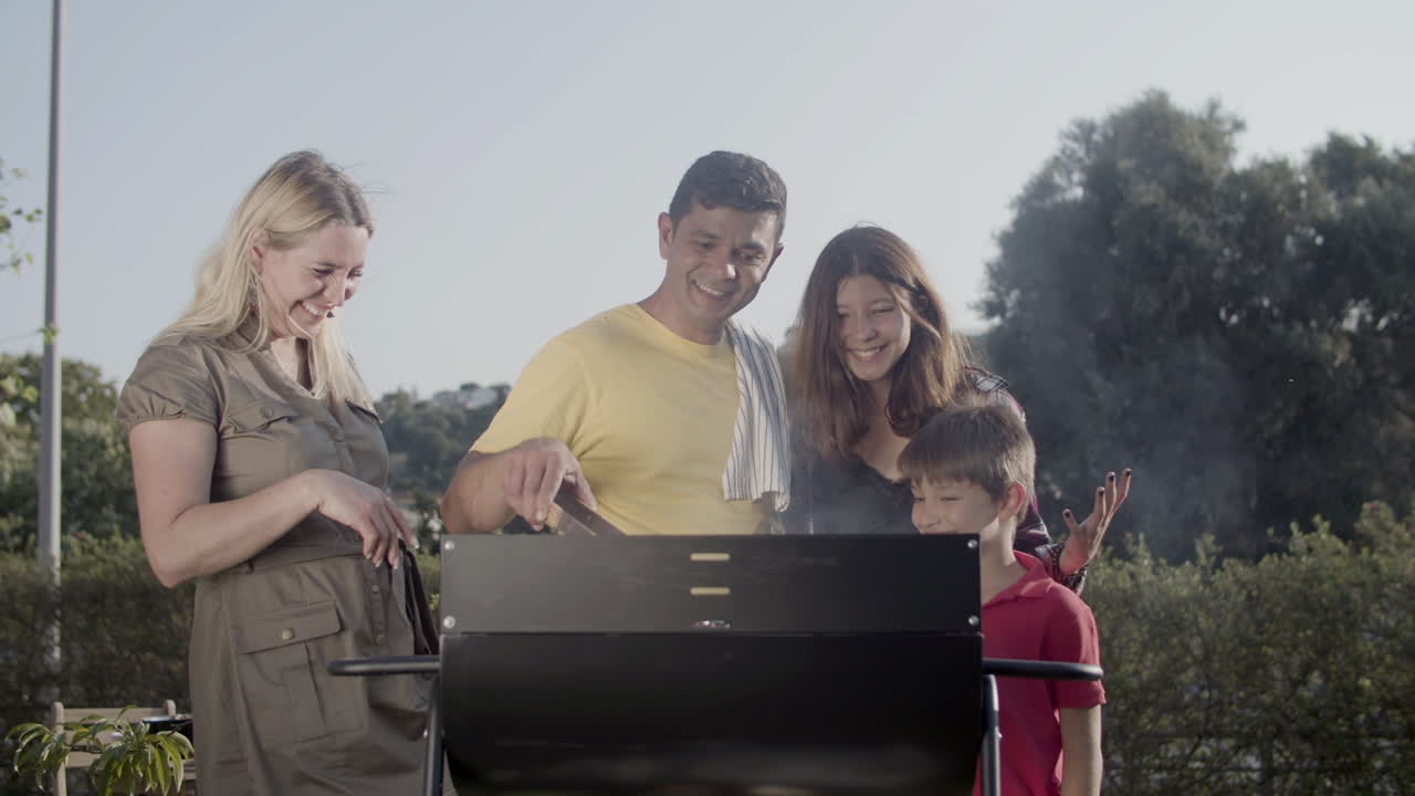 Famiglia felice in piedi insieme al barbecue che guarda la carne