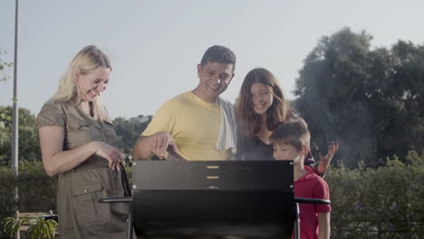 happy family standing together at barbecue grill watching meat