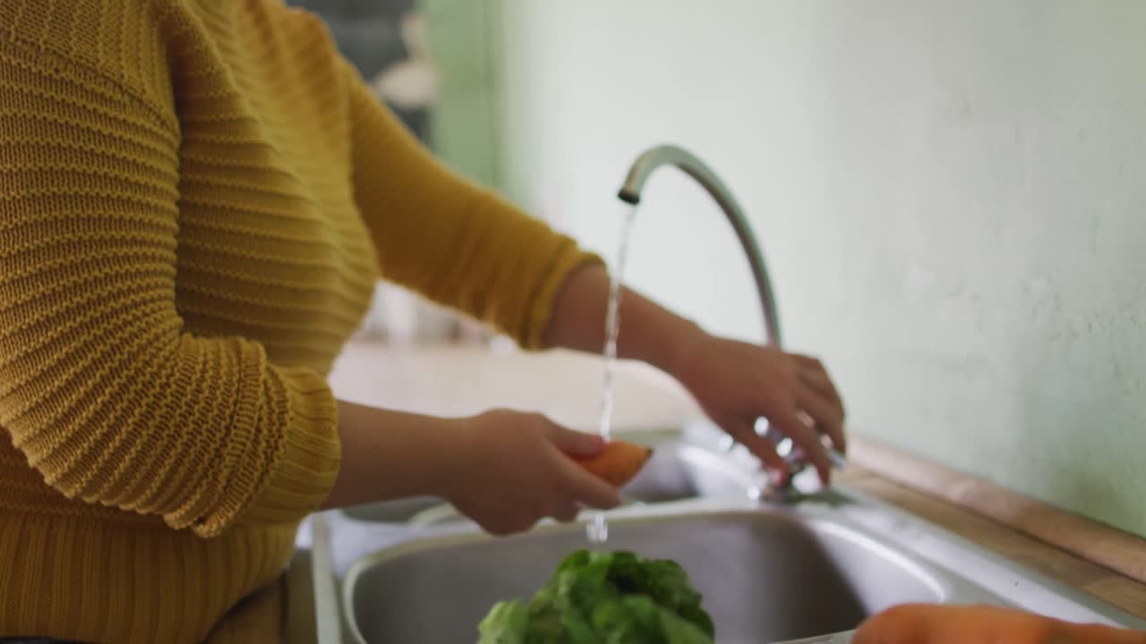 sección media de una mujer caucásica lavando verduras en la cocina