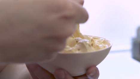 hand stirring bowl of salted caramel gelato with yellow spoon, closeup