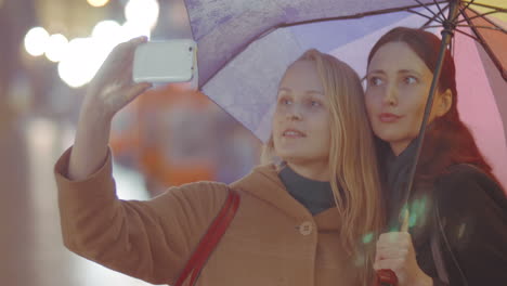 two women friends making selfie with umbrella on rainy day