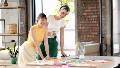 collaborating on project, two women using laptop and sticky notes in office