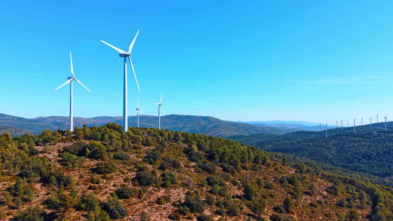 Madrid, Spagna, 8 agosto 2025: Paesaggio di parco eolico con molteplici turbine sulle creste delle montagne. Vista aerea panoramica di turbine eoliche sparse su colline verdi, cielo blu, sito di produzione di energia pulita