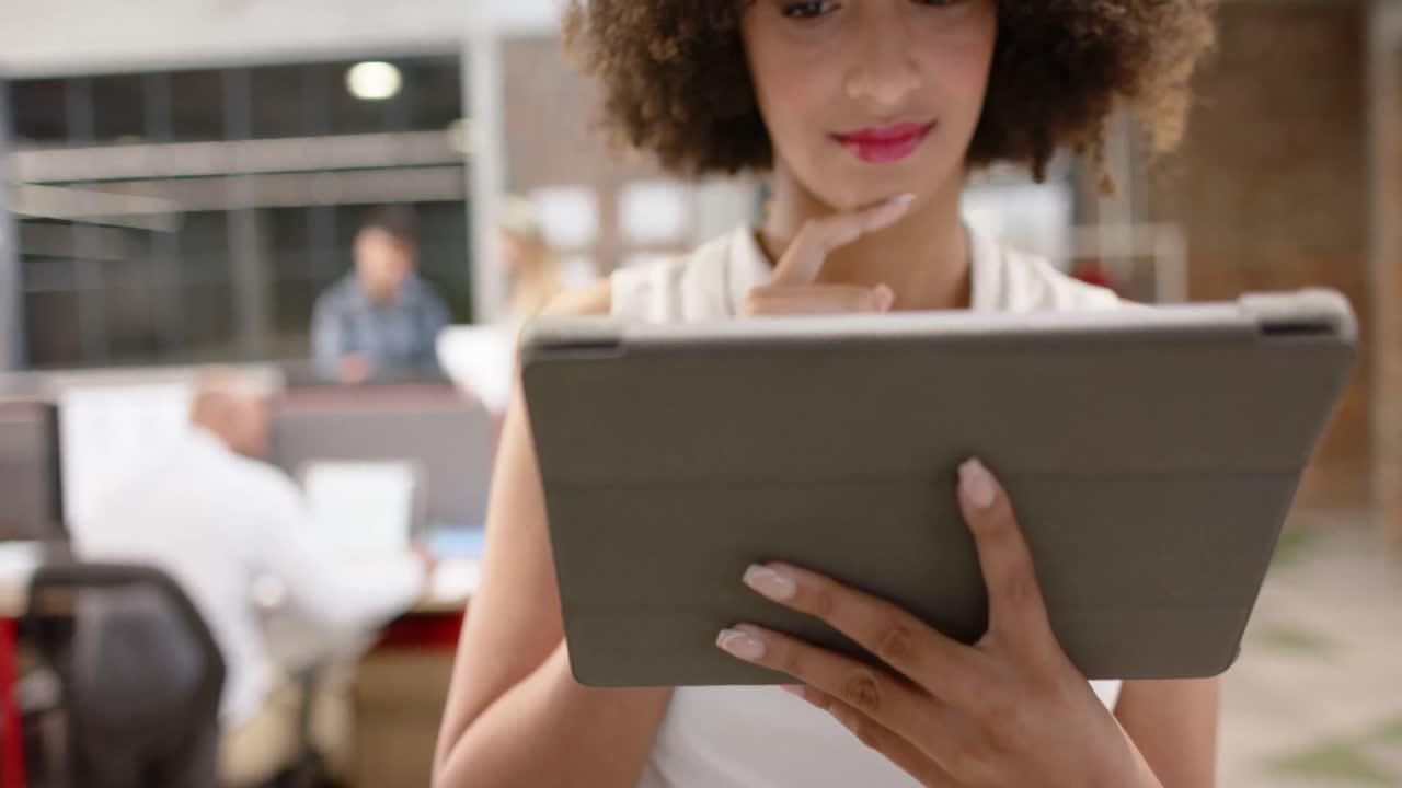 retrato de una feliz mujer de negocios creativa biracial usando una tableta en una oficina casual, en cámara lenta