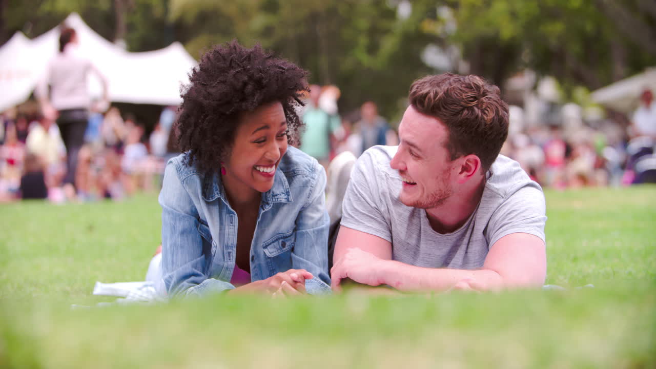 잔디 위에 누워 있는 젊은 남자 와 여자 가 한 행사 에서 이야기 하고 있다