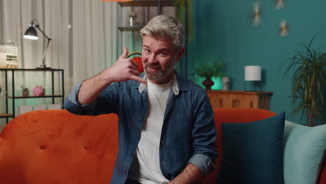 Mature-man-looking-at-camera-advertising-doing-phone-gesture-like-says-hey-you-call-me-back-at-home