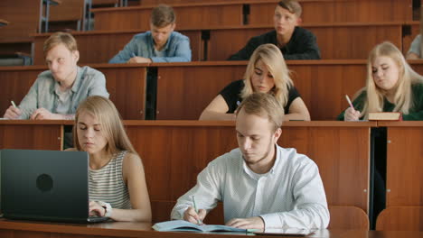 young men and women sitting in a university or college classroom write a lecture with a pen and using a laptop. institute education