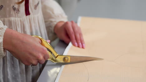 young female designer with tape-line on her neck standing in dressmaking studio and drawing lines with chalk and rule. female couturier in atelier cutting out a pattern for future clothes.