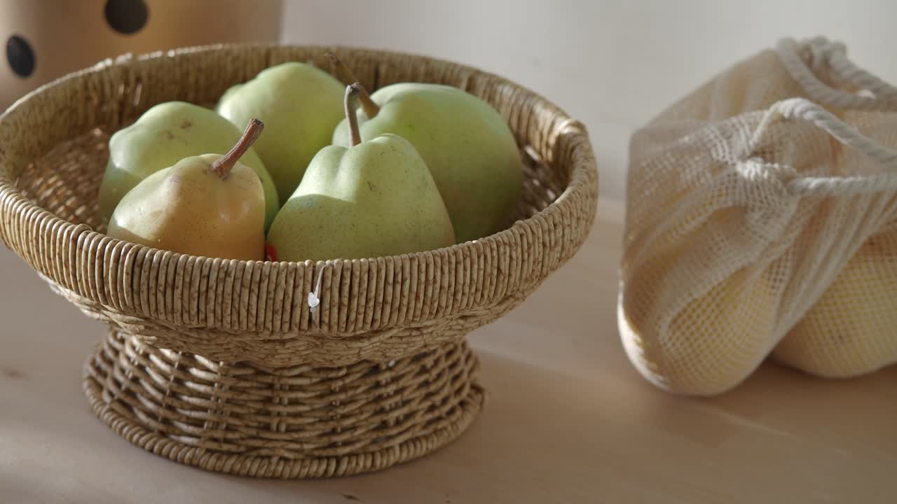 Pere fresche verdi e gialle in un cesto di vimini e un sacchetto a rete