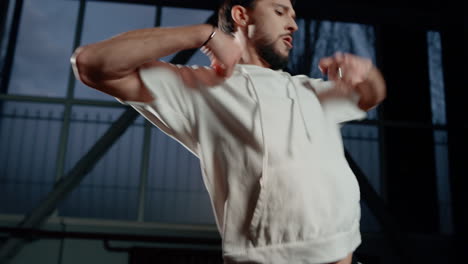 Handsome-man-dancing-in-dark-hall.-Street-style-dancer-exercising-movements.