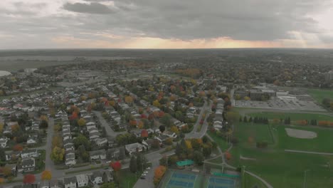 aerial footage rising from a view of a tennis court to the view of a huge sunset over a small town with sun beams showing through the clouds and lots of vehicles on turning roads