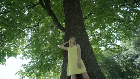 mujer con vestido amarillo bailando junto al árbol en el parque de verano
