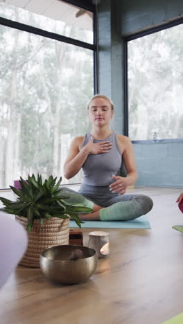 vertical video of focused diverse women meditating together on mats in yoga class, slow motion