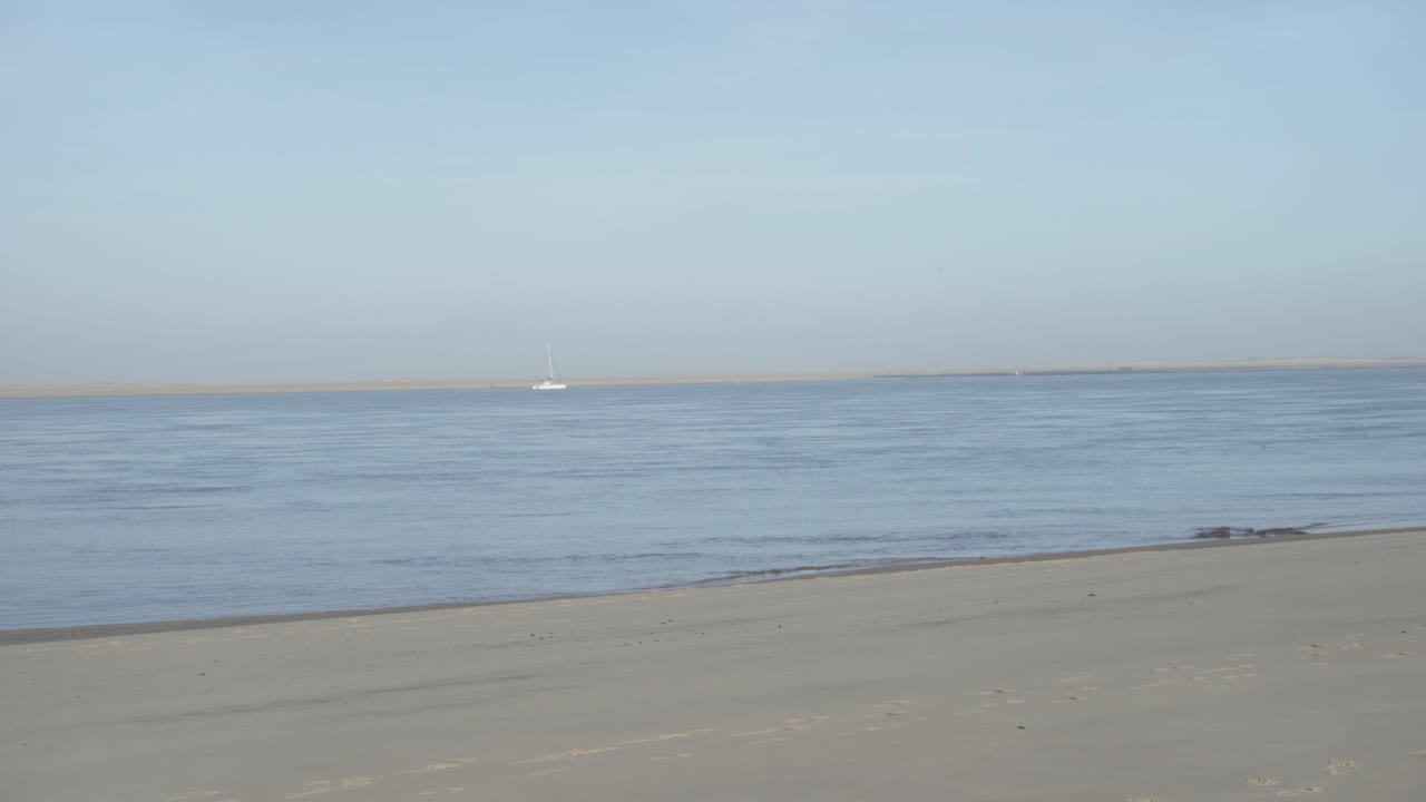 A boat is seen on the horizon from a peaceful beach in daylight