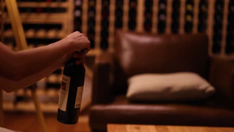 a person opens a wine bottle in a warmly lit cellar, surrounded by shelves of wine bottles and a comfortable chair