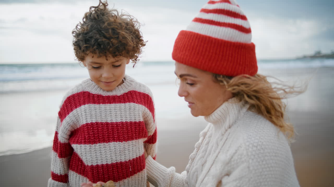 Madre premurosa bacia il figlio in primo piano sulla spiaggia dell'oceano. Figlio piccolo riccio che abbraccia la mamma.