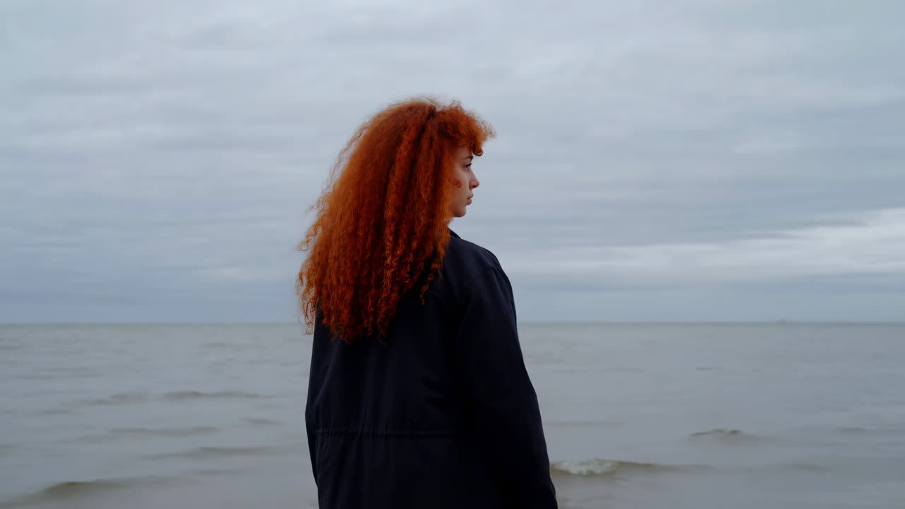 Jeune femme aux cheveux roux bouclés contemplant la mer