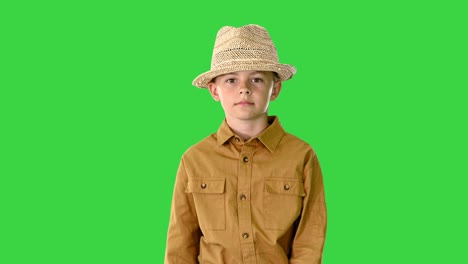 boy in a shirt adjusting his straw hat while walking and looking at camera on a green screen, chroma key