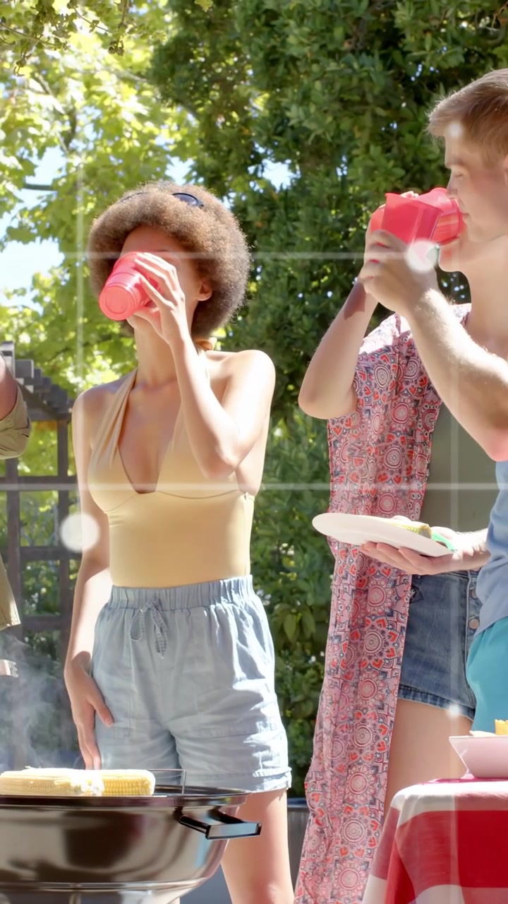 Verticale video: Hoofdgast bij de grill tilt rode beker op, nipt eraan terwijl de camera zwenkt, bereidt eten voor.