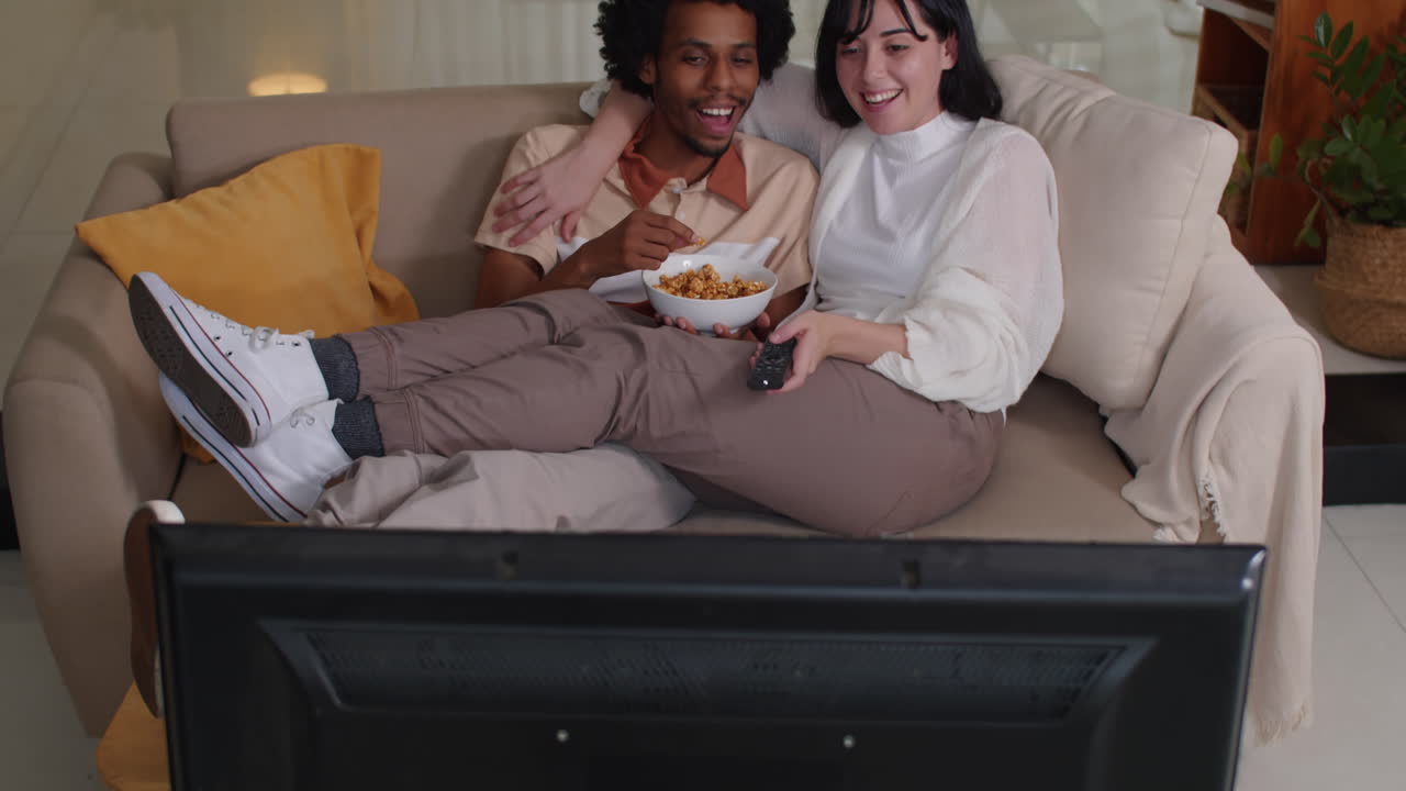 Homem e mulher carinhosos rindo enquanto assistem TV no sofá