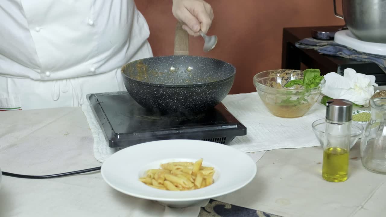 el chef coloca la pasta penne en un plato profundo y agrega verduras asadas para crear un plato de pasta norma listo para la presentación