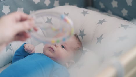 mommy shows rattle with beads to cute baby in cocoon