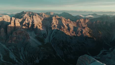 scenic aerial drone view of the rugged dolomite mountains in italy at sunrise, with a snowy foreground slope leading to the peaks