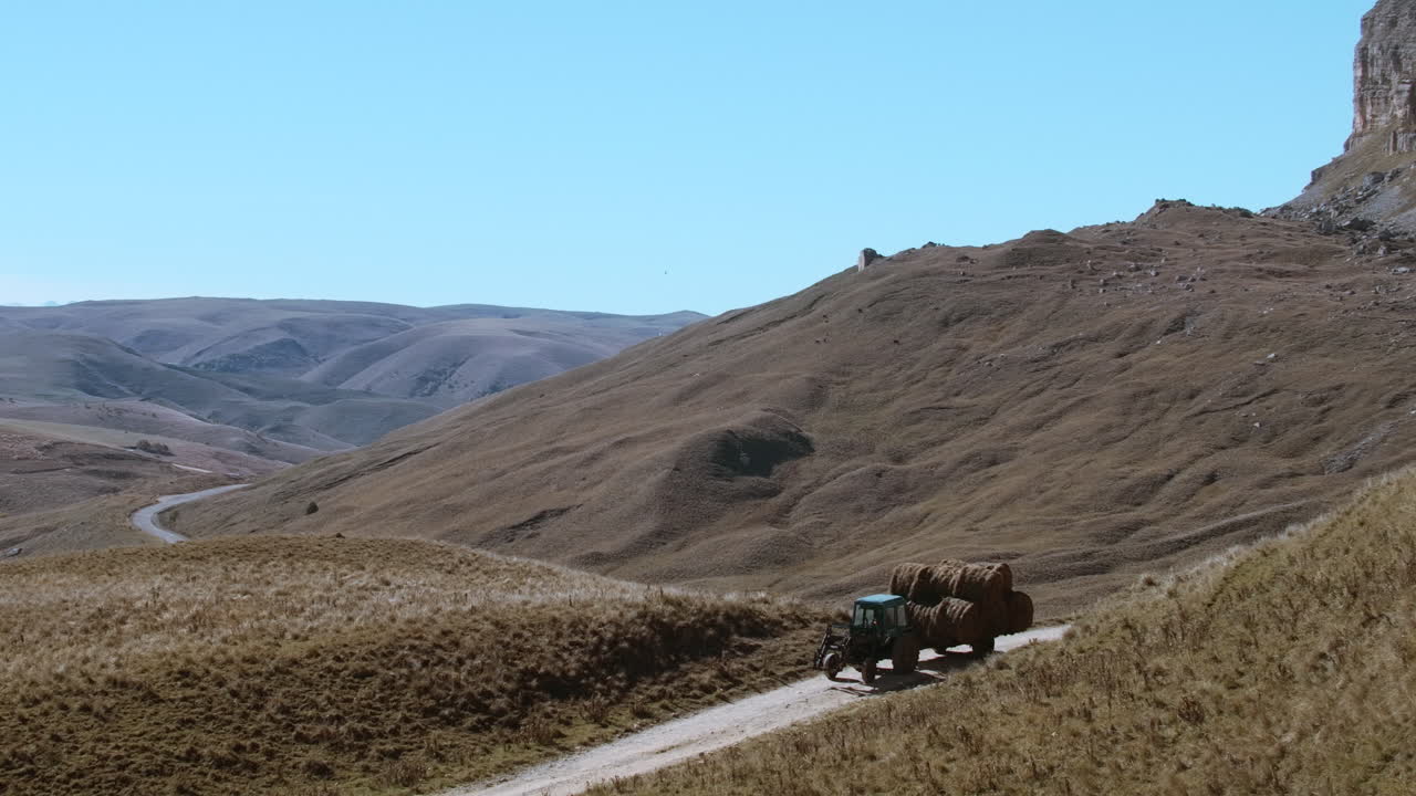 Tractor transporting hay bales through a scenic mountain valley