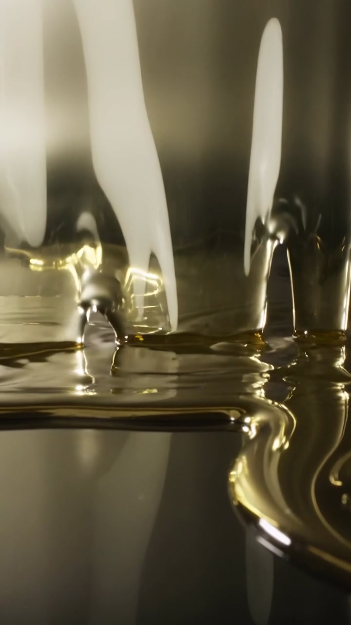 Vertical video: Flowing viscous golden liquid falling from top, forming puddle on mirror, rippling