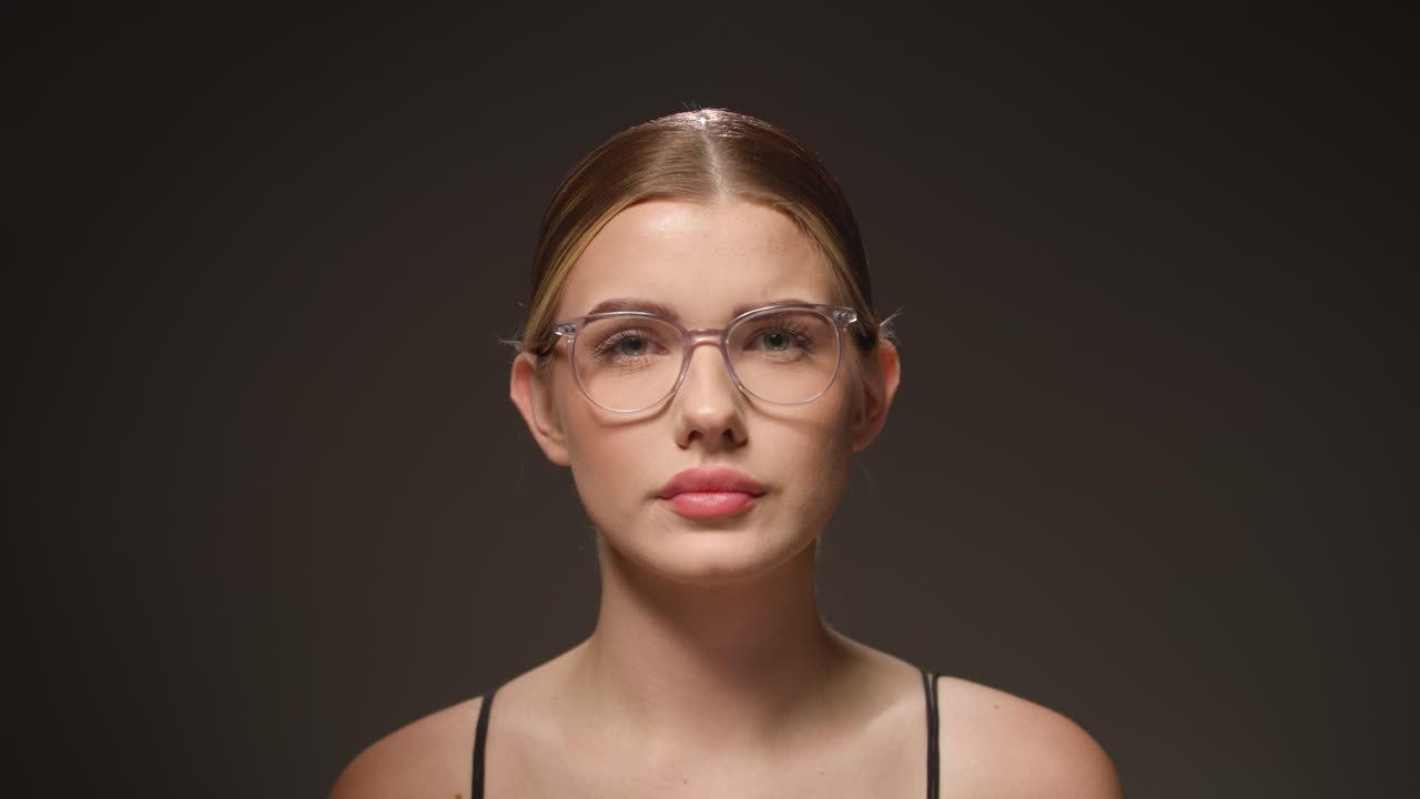 Cute woman with glasses looking confused and surprised, black background