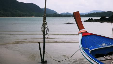 Thailändisches-Longtail-boot,-Das-Mit-Einem-Seil-Am-Strand-Entlang-Auf-Der-Insel-Koh-Lanta-In-Thailand-Mit-Wasser-Und-Wellen-Verankert-Ist