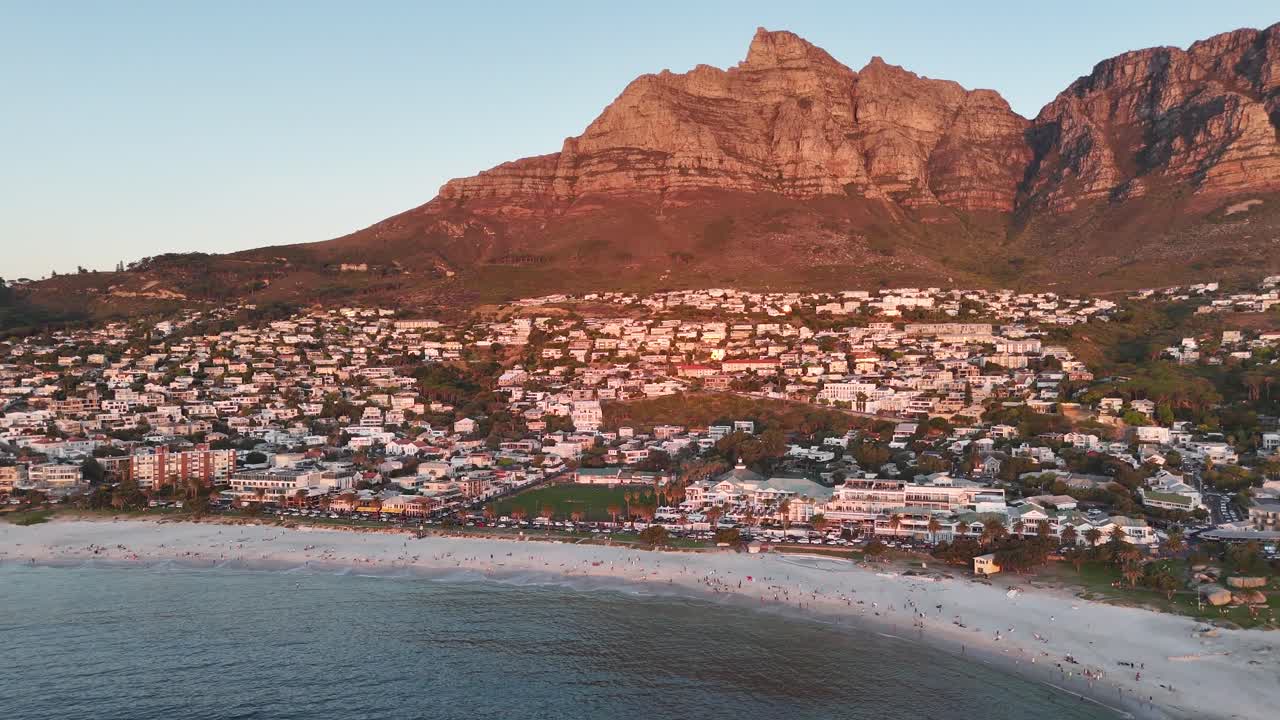 High angle drone footage approaching Lion’s Head and Atlantic coastline at sunset in Camps Bay beach with dramatic lighting at sunset , Cape Town South Africa