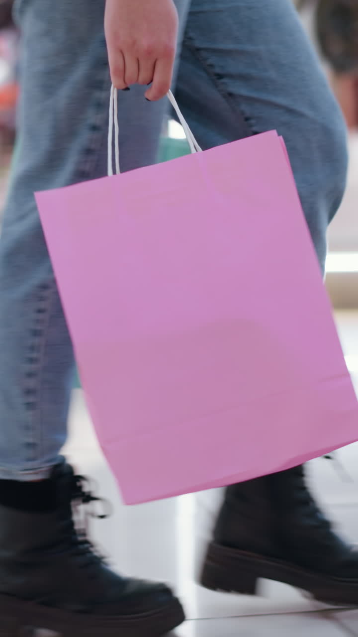 vista lateral de una persona caminando sobre azulejos elegantes con reflejos de luz, sosteniendo una bolsa de compras en una tienda minorista, las características de fondo muestran ropa con iluminación borrosa