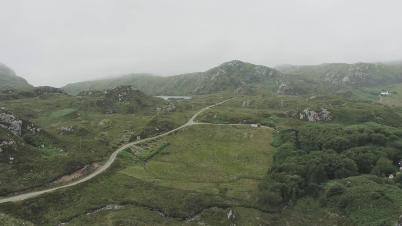 drone shot of cloudy overcast mountain range in scotland with a single track road running through it