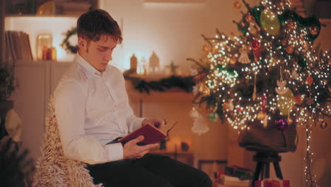 man reading book while sitting on chair at home during christmas