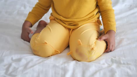 a toddler girl sits on a bed with her knees drawn on