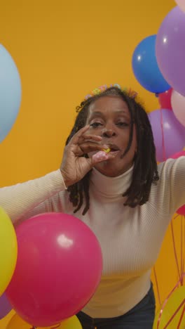 retrato vertical de estudio de video de una mujer con una cinta para la cabeza de cumpleaños celebrando con globos y soplador de fiesta 1